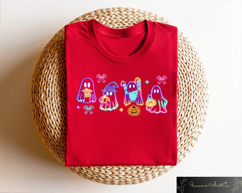 May include: Red t-shirt with a graphic of five neon ghosts holding pumpkins and candy. The ghosts are wearing hats and scarves. The graphic is surrounded by bows and stars.