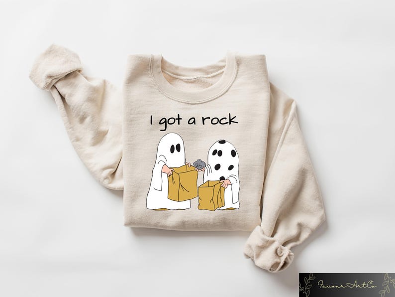 May include: A tan sweatshirt with the text "I got a rock" and a cartoon image of two ghosts trick-or-treating. One ghost is holding a rock in a brown paper bag.