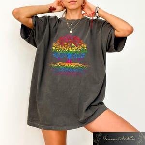 May include: Dark gray t-shirt featuring a colorful tree design in rainbow colors. The tree has a trunk, branches, leaves, and roots, all in a vibrant spectrum. The shirt is a comfortable, oversized fit.