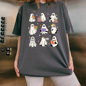 May include: Dark gray t-shirt featuring a whimsical design of nine cartoon ghosts, each holding books. The ghosts are white with black eyes and are surrounded by small stars. The shirt is a comfortable, oversized fit.