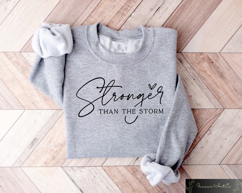 May include: Gray sweatshirt with the text "Stronger than the storm" in black cursive lettering with a small heart symbol.