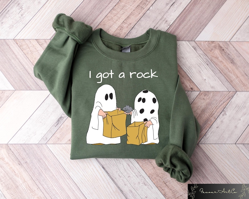 May include: Green sweatshirt with a white ghost and a black and white ghost holding brown paper bags. The text "I got a rock" is printed on the sweatshirt.