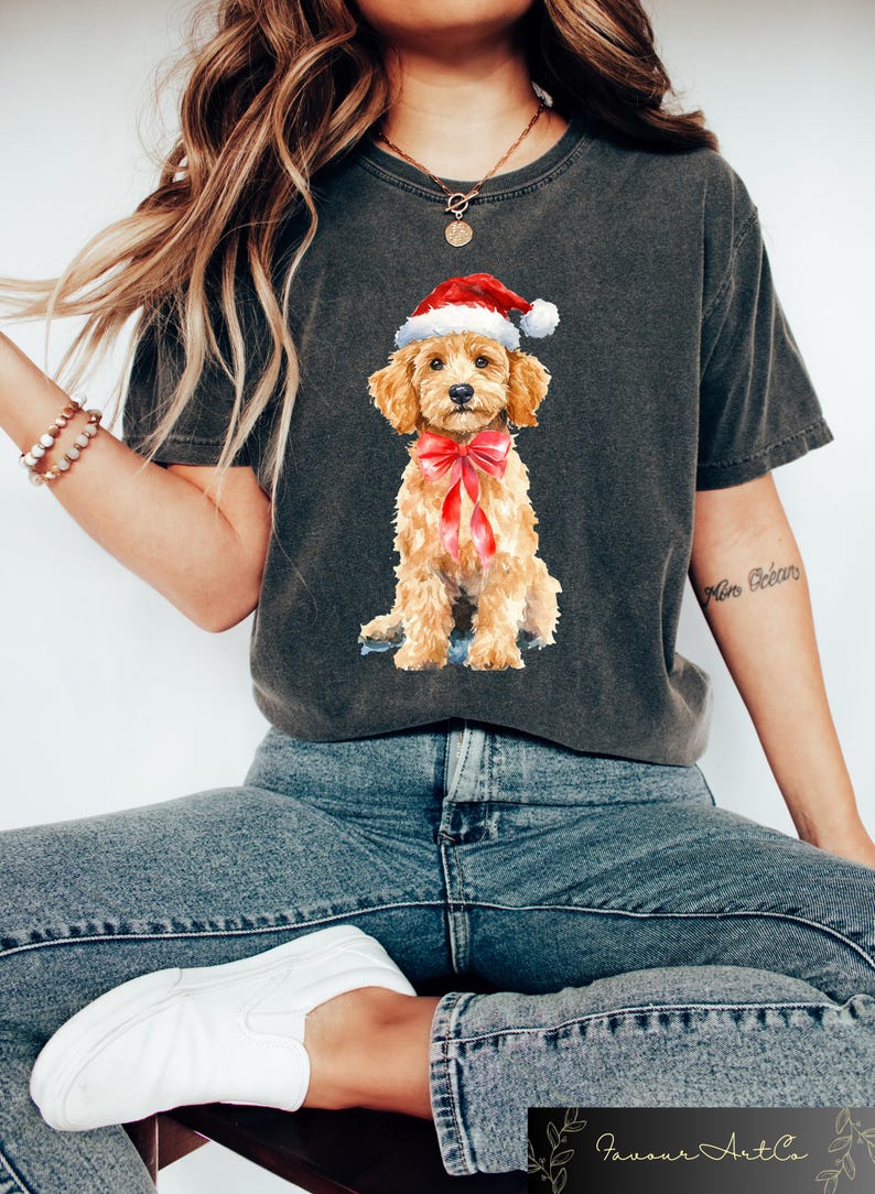 May include: Dark gray t-shirt featuring a watercolor illustration of a golden doodle puppy wearing a Santa hat and a red bow. The puppy is sitting, with a sweet expression. The shirt is a comfortable, casual style.