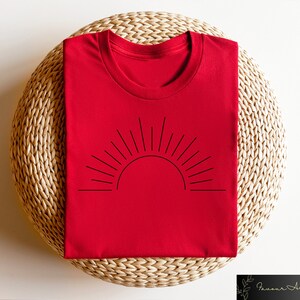 May include: Red t-shirt with a black line drawing of a sun with rays on the front.