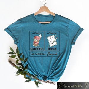 May include: Teal blue t-shirt with a graphic design of a coffee cup and a checklist with a pencil. The text reads "First Coffee, Then Data, I am earning a: Break".