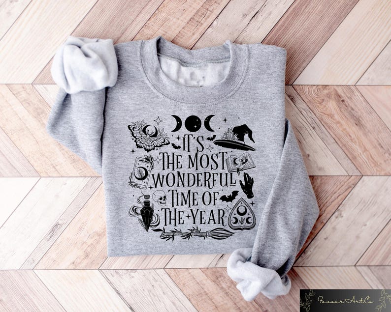 May include: Gray sweatshirt with a black and white graphic print of a witch's hat, a crescent moon, a book, a potion bottle, a skull, and a pentagram. The text on the sweatshirt reads "It's the most wonderful time of the year."