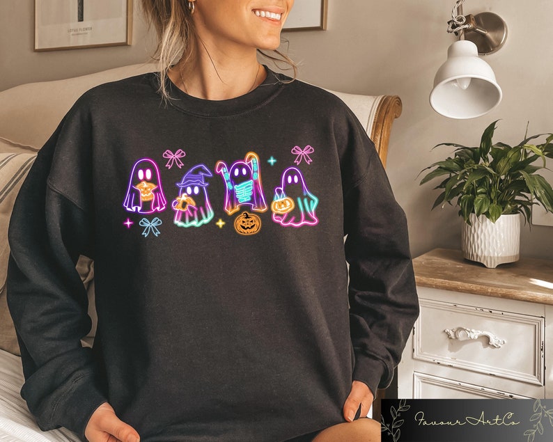 May include: Black sweatshirt with a neon design of five ghosts holding pumpkins and candy. The ghosts are wearing hats and masks.