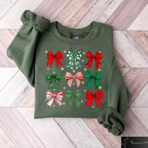 May include: A green sweatshirt with a Christmas-themed design featuring multiple red and green bows with gold accents.