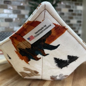 Puede incluir: Un salvamanteles cuadrado de tela con fondo crema y un estampado de árboles y animales marrones, naranjas y verde azulado. La etiqueta dice "Handmade by FLPatriotProvisions" con una pequeña bandera americana.