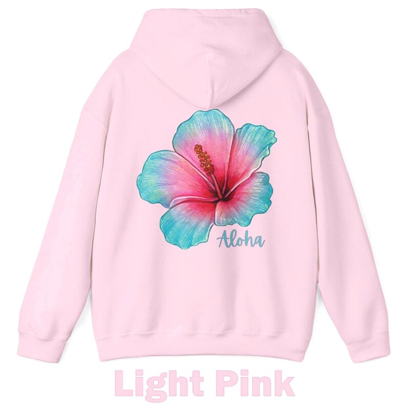 May include: A light pink hooded sweatshirt featuring a large, colorful hibiscus flower graphic on the back. The flower displays a gradient of pink, magenta, and teal blue tones. Below the flower, the word Aloha is printed in a teal script font.