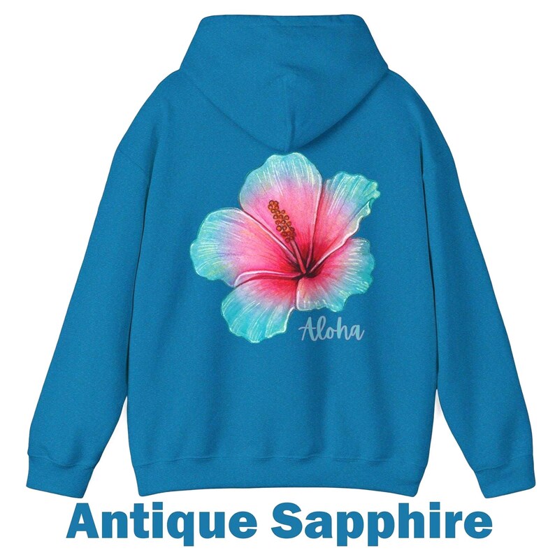May include: An antique sapphire blue hooded sweatshirt featuring a large, vibrant hibiscus flower graphic on the back. The flower displays a gradient of pink, magenta, and teal colors. The word Aloha is printed in a white script font below the flower.