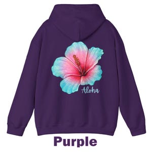 May include: A deep purple hooded sweatshirt featuring a large, vibrant hibiscus flower graphic on the back. The flower displays a gradient of pink and light blue petals with a yellow stamen. The word Aloha is printed in white script below the flower.