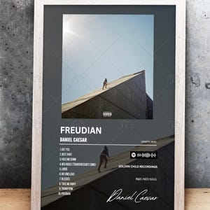 Op de afbeelding: Ingelijste albumkunstprint voor "Freudian" van Daniel Caesar. De afbeelding toont een persoon die op het schuine dak van een gebouw loopt. De albumtitel en tracklist worden in witte tekst op een donkere achtergrond weergegeven.