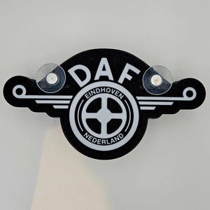 May include: Black and white DAF logo with the words "Eindhoven" and "Nederland" on a black background. The logo has two suction cups on the top.