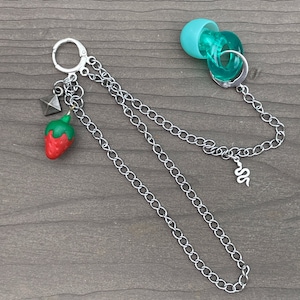May include: A silver chain necklace with a charm of a red strawberry, a silver pyramid, and a silver snake. The necklace also has a turquoise blue charm with a silver ring.