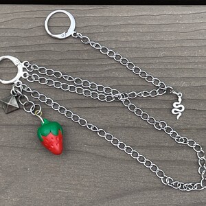May include: A silver chain necklace with a strawberry charm, a small pyramid charm, and a snake charm.