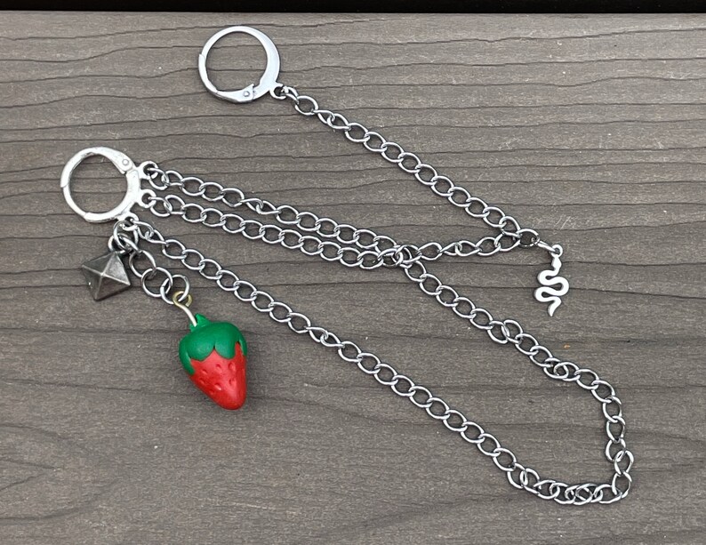 May include: A silver chain necklace with a strawberry charm, a small pyramid charm, and a snake charm.
