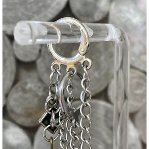 May include: Silver hoop earrings with multiple chain and charm accents, including a green bead.