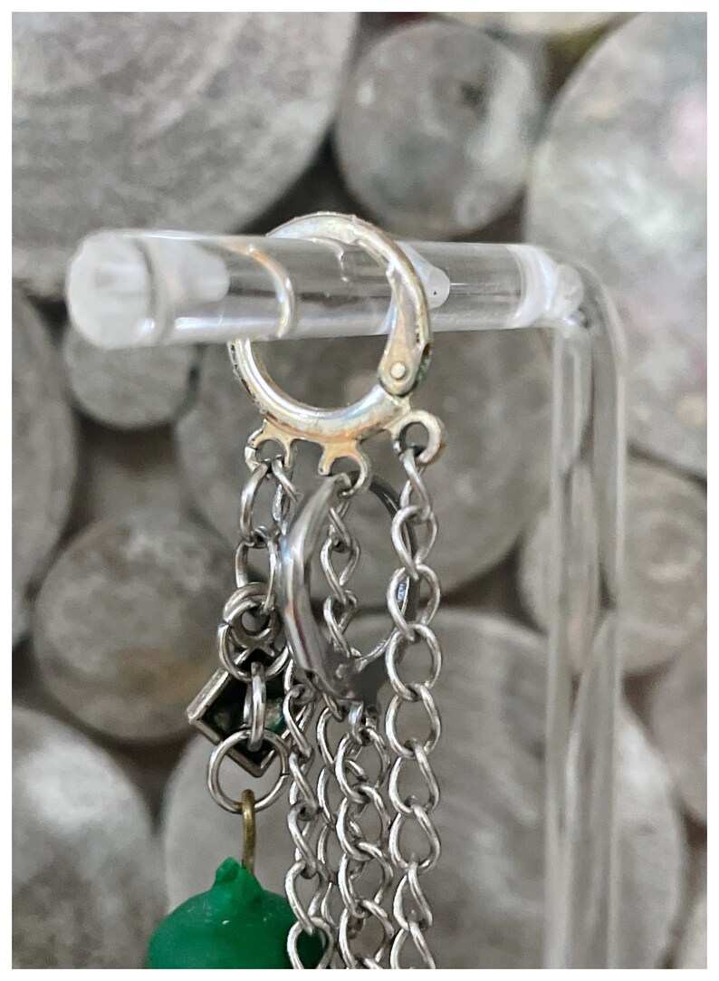 May include: Silver hoop earrings with multiple chain and charm accents, including a green bead.