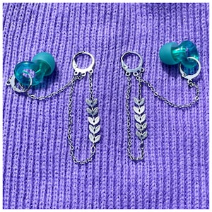 Puede incluir: Un par de pendientes de cadena plateada con abalorios en forma de hoja. Los pendientes están unidos a unos pendientes de aro de color azul turquesa.