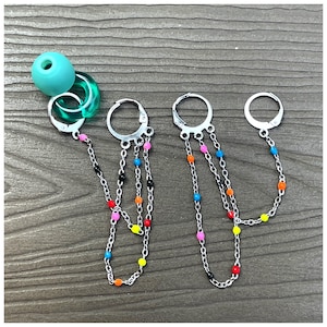 Puede incluir: Tres pares de pendientes de aro de plata con múltiples cadenas adjuntas. Cada cadena tiene cuentas de colores en rosa, azul, amarillo, naranja y negro.