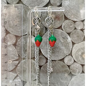 May include: A pair of silver chain earrings with a strawberry charm and a silver pyramid charm. The earrings are approximately 2 inches long.