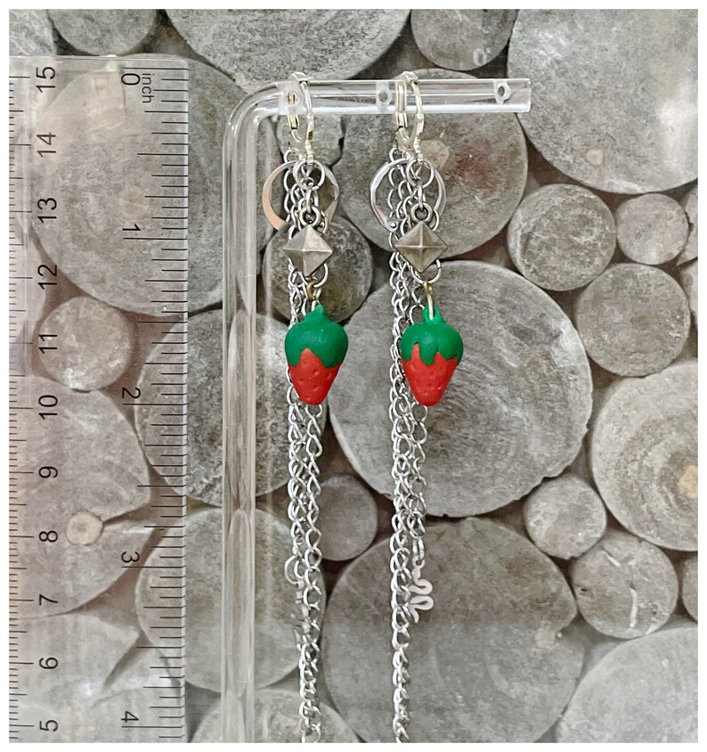 May include: A pair of silver chain earrings with a strawberry charm and a silver pyramid charm. The earrings are approximately 2 inches long.