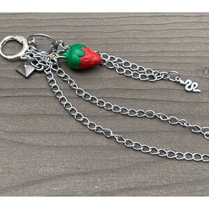 May include: A silver chain with a red and green strawberry charm, a silver snake charm, and a silver pyramid charm.