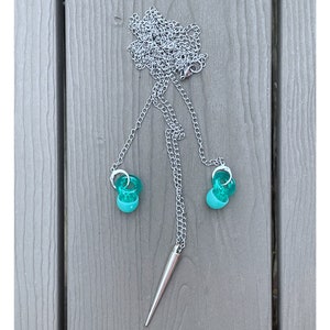 May include: A silver chain necklace with a silver spike pendant and two turquoise colored glass beads at the ends.
