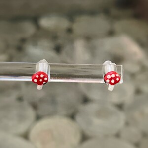 May include: A pair of red and white mushroom earrings. The earrings are small and have a white stem and a red cap with white dots.