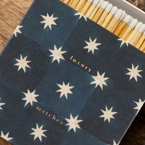 May include: A box of matches with a navy blue and white star pattern. The words "luxury" and "matches" are printed in gold. The matches are wooden with white tips.