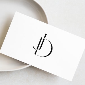 May include: A white card with a black monogram of the letters "JD" in a stylized font.