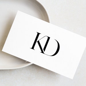 May include: A white card with the letters "KD" in black on a white oval plate.