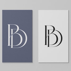 Könnte beinhalten: Zwei rechteckige Karten, eine in gedämpftem Blau und die andere in Weiß, jeweils mit einem stilisierten Monogramm der Buchstaben "B" und "D". Das "B" ist ein hoher, eleganter Serifenbuchstabe, der mit einem abgerundeten "D" verschlungen ist.