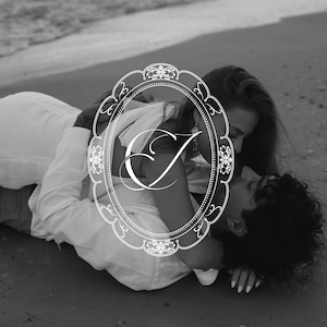 Puede incluir: Fotografía en blanco y negro de una pareja abrazándose en una playa de arena. La imagen está enmarcada por un borde ovalado decorativo con la letra "C" en el centro. La pareja viste ropa blanca.