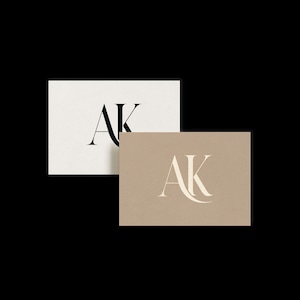 May include: Two business cards with the letters "AK" in a serif font. One card is off-white with black lettering, and the other is tan with light beige lettering. The cards are displayed against a black background.