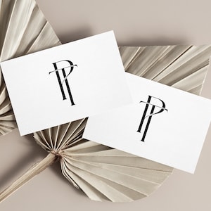 May include: Two white business cards with a black monogram logo featuring the letters "P" and "T" are displayed on a beige background. The cards are arranged on top of dried palm leaves, creating a minimalist and elegant aesthetic.