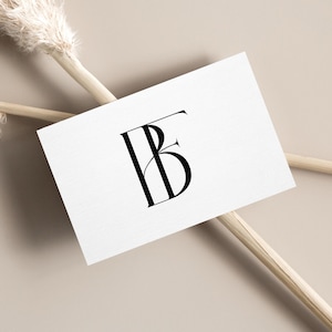 Puede incluir: Una tarjeta de visita blanca con un monograma negro de las letras "FB" en una fuente elegante con serif. La tarjeta está sobre un fondo beige neutro, con hierba ornamental seca y un palo de madera.