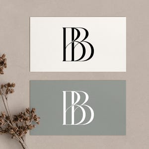 Op de afbeelding: Twee visitekaartjes met de letter "B" in een gestileerd lettertype. Eén kaart is wit met een zwarte "B", de andere is grijs met een witte "B". Een takje gedroogde bloemen staat in de hoek.