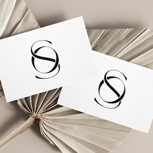 May include: Two white cards with a black stylized letter "S" logo on each card. The cards are placed on a dried palm leaf.