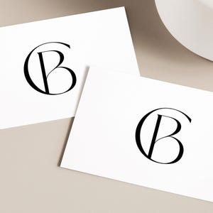 Könnte beinhalten: Zwei weiße Karten mit einem schwarzen Monogramm des Buchstabens "B" in einem Kreis auf jeder Karte.