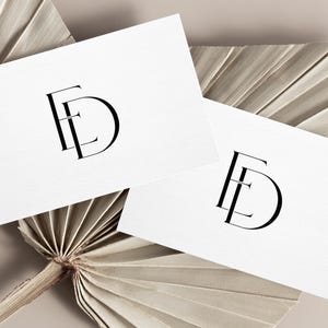 May include: Two white business cards with a black FD monogram are displayed on a neutral-toned background. The cards are arranged at an angle, showcasing the elegant logo design. The background features dried palm leaves.
