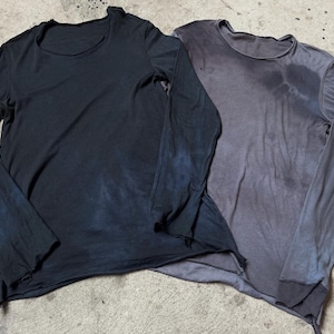 Puede incluir: Dos camisas de manga larga. Una es azul marino oscuro con detalles en azul, la otra es gris con detalles en gris más oscuro. Ambas camisas tienen un aspecto desgastado con bordes sin rematar y cuello redondo.