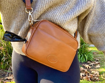 Tan faux leather dog walking bag with gold hardware. Includes built-in waste bag compartment.