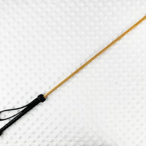 Könnte beinhalten: Eine Reitgerte aus Holz mit einem schwarzen Ledergriff und einer Schlaufe.