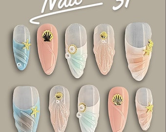 Puede incluir: Un conjunto de diez uñas postizas etiquetadas como Nail 31, con colores pastel azul, rosa y blanco, texturas de conchas esculpidas, dijes de estrellas de mar doradas, detalles de conchas doradas y pequeñas perlas blancas en dos filas.