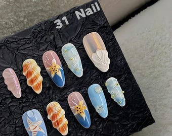 Puede incluir: Un conjunto de 10 uñas postizas con diferentes diseños inspirados en el océano. Los diseños incluyen conchas marinas, estrellas de mar y perlas. Las uñas están sobre un fondo negro con el texto "31 Nail" escrito en blanco.