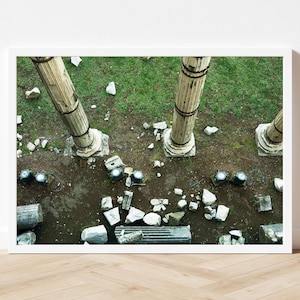 May include: An aerial view of three broken stone columns lying on a grassy field. The columns are made of white stone and have a rough texture. There are pieces of broken stone scattered around the columns.