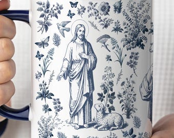 May include: White ceramic mug with a blue interior and handle. The mug features a blue and white illustration of Jesus, a lamb, and floral and butterfly motifs. The design is reminiscent of classic toile patterns.