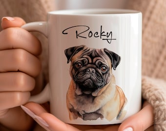 May include: White ceramic mug featuring a watercolor illustration of a pug dog. The mug has the name "Rocky" written in a script font. The pug is depicted with brown and black fur. The mug is held by a person.